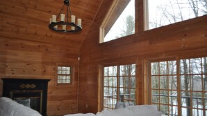 Ein Holzblockhaus-Innenraum mit Kamin, einer Couch und großen Fenstern, die einen Blick auf Bäume bieten.