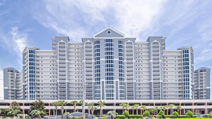 A multi-story hotel with a central atrium, balconies, and a parking area with palm trees. - Lighthouse 910 - Perfect Spot in the Middle of the Building (Gulf Shores)