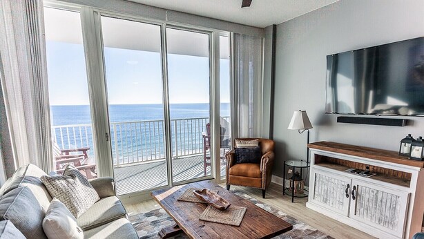 A living room with a sofa, armchair, coffee table, and a TV mounted on the wall. - Lighthouse 910 - Perfect Spot in the Middle of the Building (Gulf Shores)
