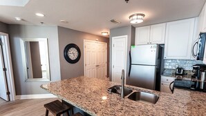 A modern kitchen with granite countertops, stainless steel appliances, and wooden stools. - Lighthouse 910 - Perfect Spot in the Middle of the Building (Gulf Shores)