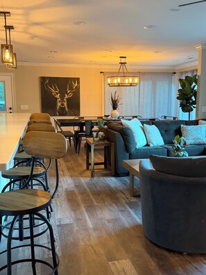 A modern living room with a dining area, a large painting, and a chandelier.