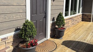 A house with a dark gray front door, two potted plants, and a wooden deck.