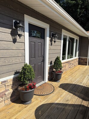 A house with a dark gray front door, two potted plants, and a wooden deck.