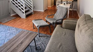 Amplia sala de estar con sofá, una mesa de centro y una mesa de comedor. Se observa una escalera con barandilla que conduce a otro nivel. Se ve un ventilador de techo.