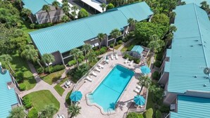 An aerial view of a resort with a central swimming pool surrounded by lounge chairs and umbrellas, with multiple buildings featuring blue roofs. - Siesta Key Beach IDEAL LOCATION BEACH, VILLAGE, HEATED POOL (Siesta Key)