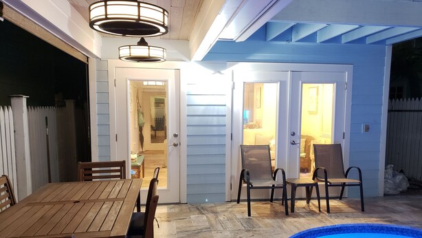 An outdoor patio area with a wooden table and chairs, a swimming pool, and a ceiling fan.