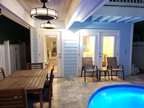 Área de varanda externa com mesa e cadeiras de madeira, piscina e ventilador de teto.