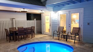 A backyard with a swimming pool, a dining table with chairs, and a covered patio area.