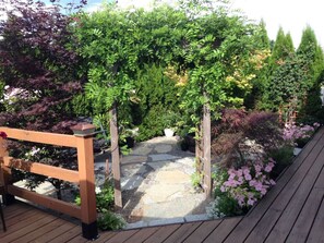 A wooden deck leading to a stone pathway surrounded by lush greenery and flowering plants. - Suite Getaway at Green Bluff w/hot tub, BBQ,  private garden and views! (Colbert)