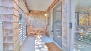 Eine überdachte Terrasse mit Tisch und Stühlen, Wände mit Holzverkleidung und eine Glastür, die in einen Garten führt.