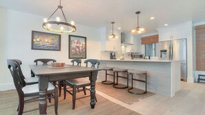 A modern kitchen with a central island, pendant lights, and a dining area with a wooden table and chairs. - Spectacular 1 Bedroom, Oceanfront Villa! BRAND NEW RENOVATION!! (Kiawah Island)
