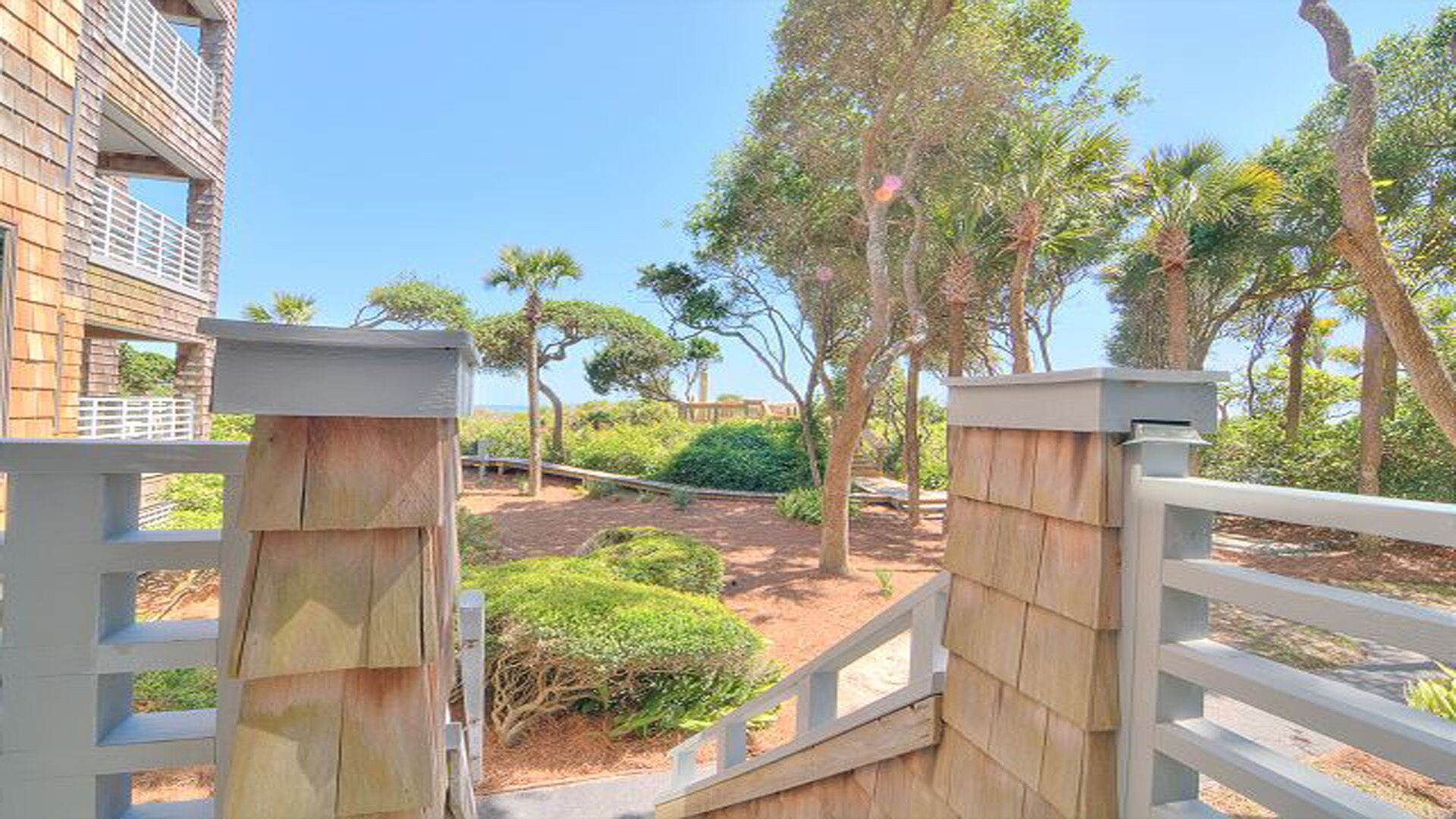 A gated entrance with a wooden fence and a pathway leading to a landscaped area with trees and shrubs.