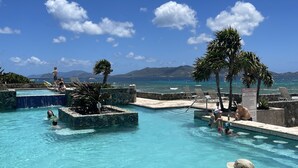 Un espace piscine avec une eau d’un bleu limpide, des chaises longues et des palmiers.