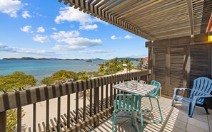 A balcony with a view of the sea, a table with chairs, and a wooden railing. - Sapphire Outlook Villa : Beachfront 2-story Top Floor Villa on Sapphire Beach (St. Thomas)