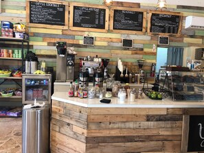 Un comptoir de café avec un tableau affichant les différents types de café et leurs prix, une machine à café, ainsi que divers condiments et ingrédients.