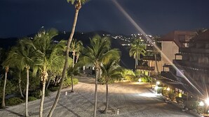 Une vue nocturne d’un complexe hôtelier avec des palmiers, une plage et des bâtiments dotés de balcons.