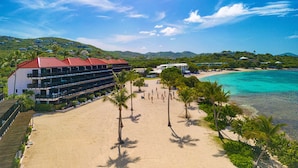 Un hôtel situé en bord de mer, doté de nombreux balcons, d’une plage de sable fin et d’une eau turquoise et cristalline.