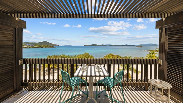 Une terrasse en bois avec une table et des chaises, offrant une vue sur la côte et un ciel dégagé.