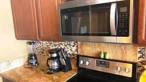 Una cocina con gabinetes de madera, microondas de acero inoxidable, cafetera y estufa.