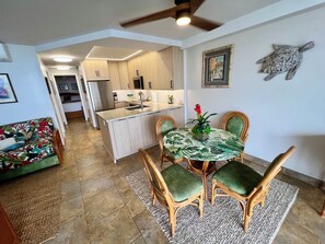 Une cuisine moderne avec des meubles en bois et un îlot central, un coin repas avec une table ronde et des chaises, et un salon avec un canapé et un élément décoratif mural.