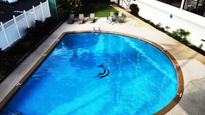 Una piscina rectangular con un cartel de prohibido bucear, rodeada por un deck de concreto y una cerca blanca.
