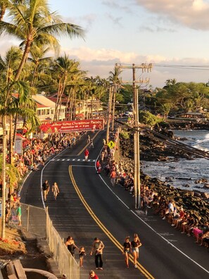 A coastal road lined with palm trees and a crowd watching a parade.