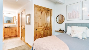 Un dormitorio con una cama, un armario de madera, un espejo y cuadros en la pared.