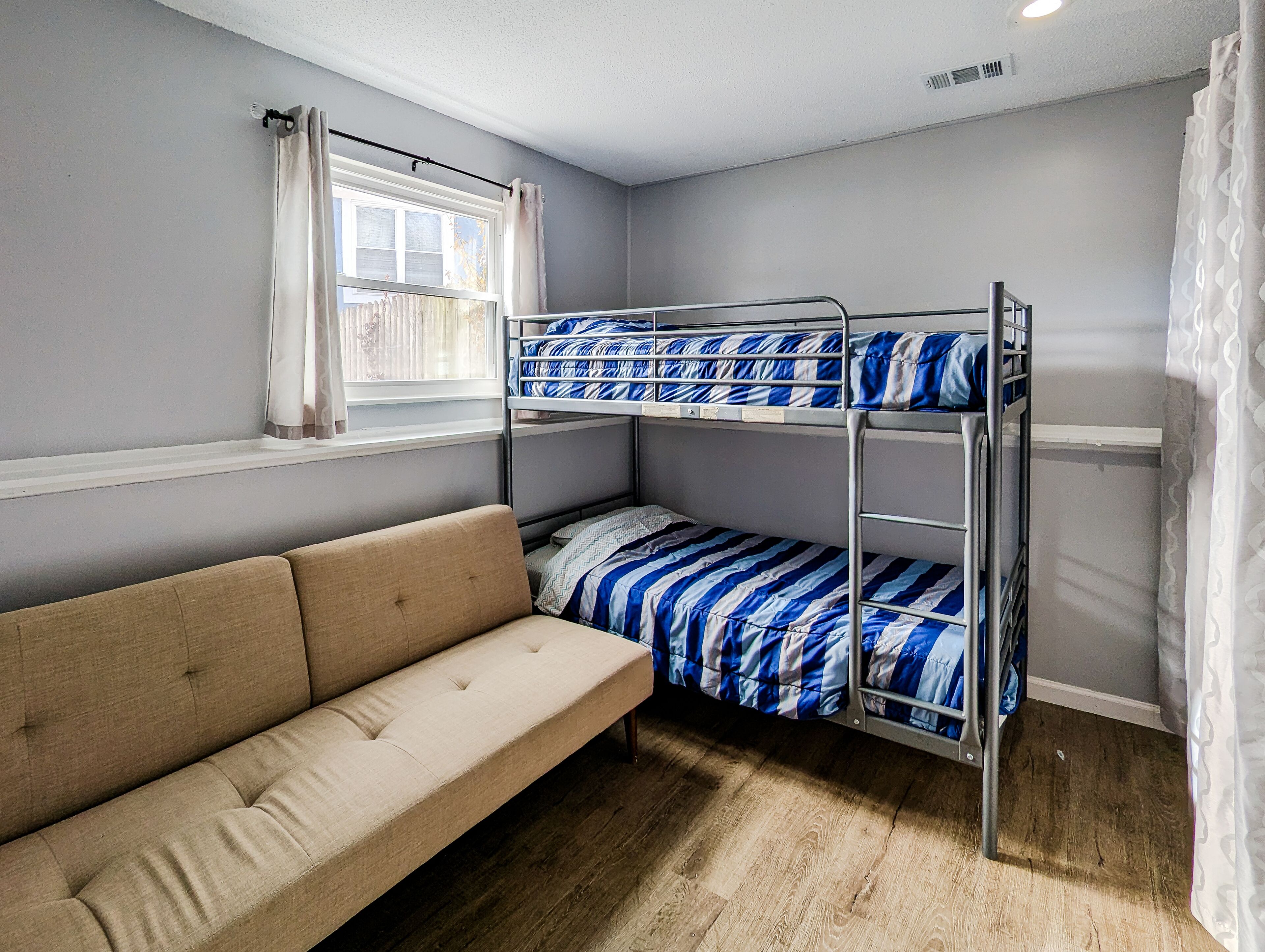 Un lit superposé avec une literie bleue et blanche, un canapé beige et une fenêtre avec des rideaux.