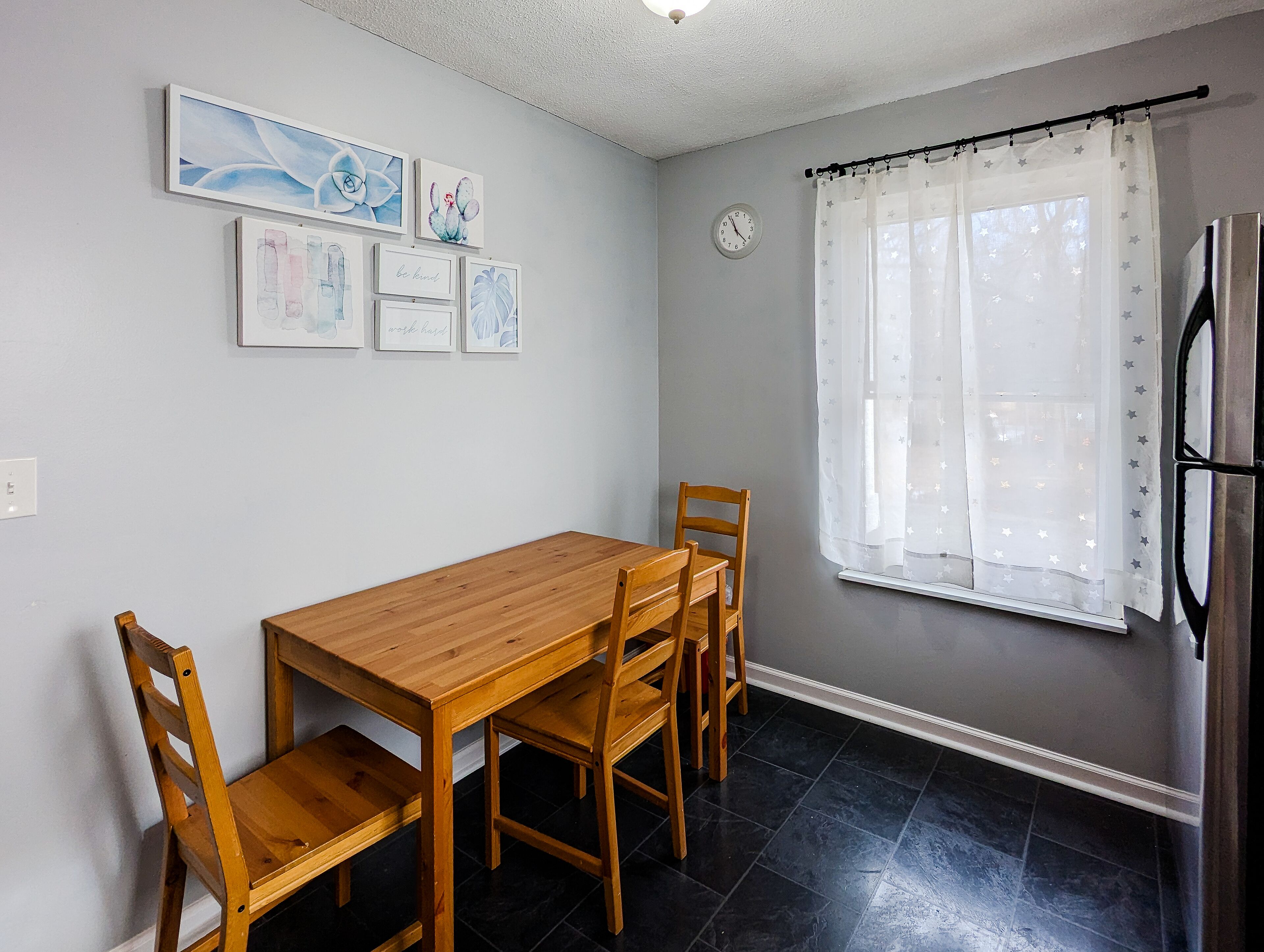 Un comedor con mesa y sillas de madera, un reloj en la pared y obras de arte.