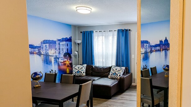 A living room with a sofa set, a dining table, and chairs. There is a mural of a cityscape on the wall. - Nice and cozy duplex close to everything in KC! (Overland Park)