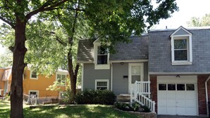 A two-story residential building with a front porch, a garage, and a well-maintained lawn. - Nice and cozy duplex close to everything in KC! (Overland Park)