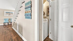 A hallway with a wooden floor, a staircase, and a door leading to a laundry room. - Canal House 2 short blocks to the beach with beach access! (Ocean Isle)