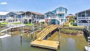 A waterfront property with a wooden dock, multiple buildings with balconies, and a clear sky. - Canal House 2 short blocks to the beach with beach access! (Ocean Isle)