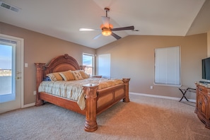 A bedroom with a wooden bed, a ceiling fan, a television, and a view through the window.