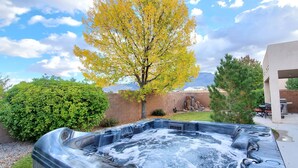 A hot tub in a backyard with a tree, a brick wall, and a mountain in the background.