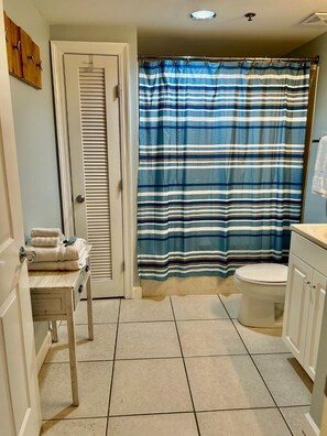 Een badkamer met een gestreept douchegordijn, een toilet en een klein tafeltje met handdoeken.