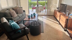 Un salon comprenant un canapé, une table basse, un pouf et un meuble pour la télévision.