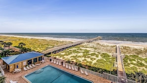Ein Hotel am Strand mit Pool, Liegestühlen und einer Pier, die ins Meer ragt.