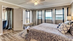 Ein Schlafzimmer mit einem großen Bett, einem Deckenventilator, Blick auf den Ozean und einem Balkon mit Vorhängen.