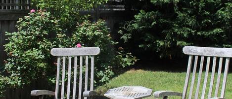 Une terrasse avec deux chaises en bois et une petite table, entourée d’une clôture en bois et de verdure.