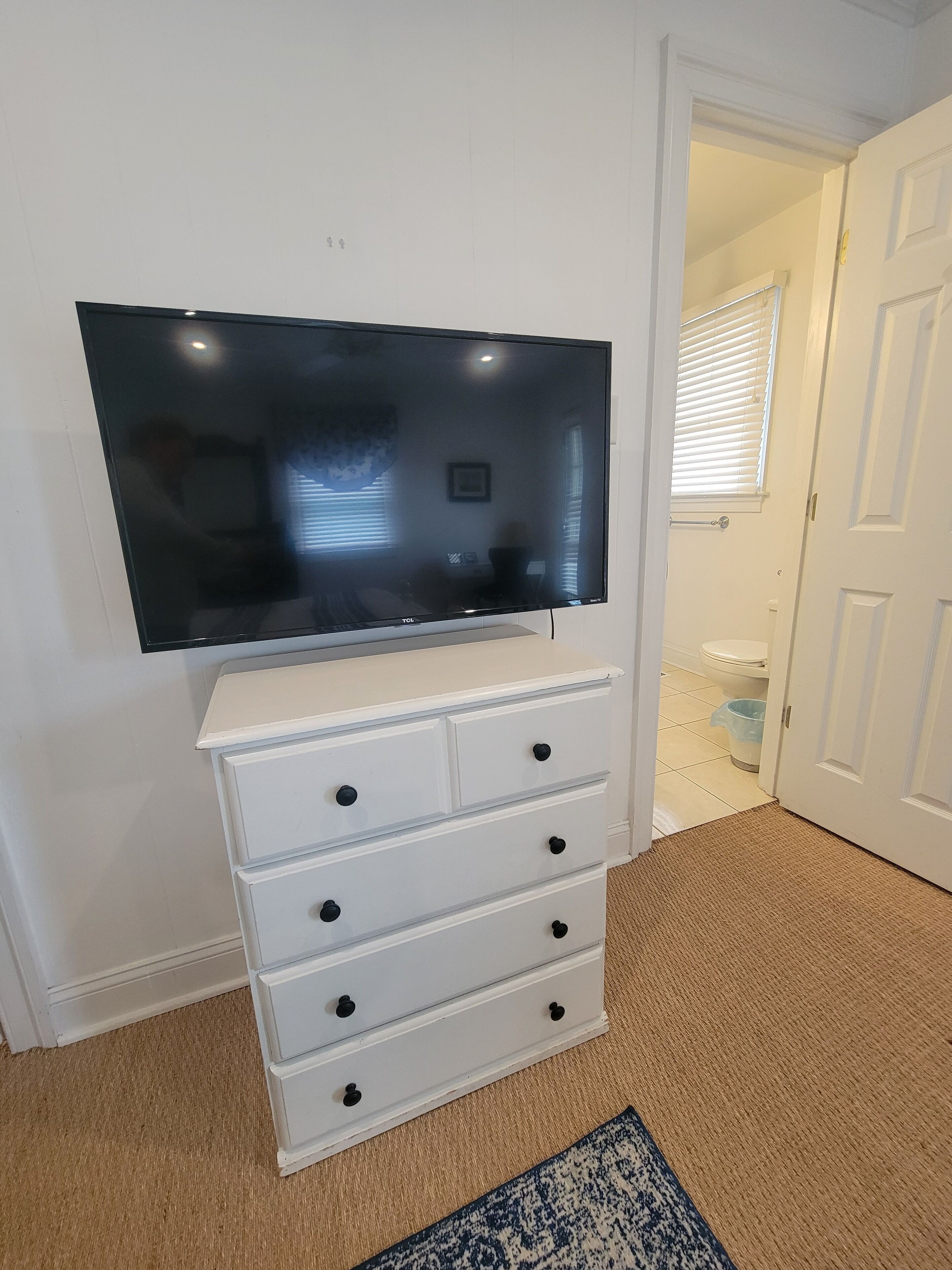 A white dresser with drawers and a flat-screen TV mounted above it.