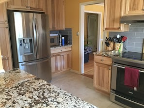 A kitchen with stainless steel appliances, wooden cabinets, granite countertops, and a tiled backsplash.
