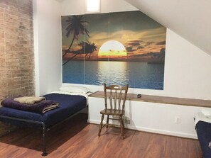 A bedroom with a bed, a chair, and a large wall mural of a sunset over water.