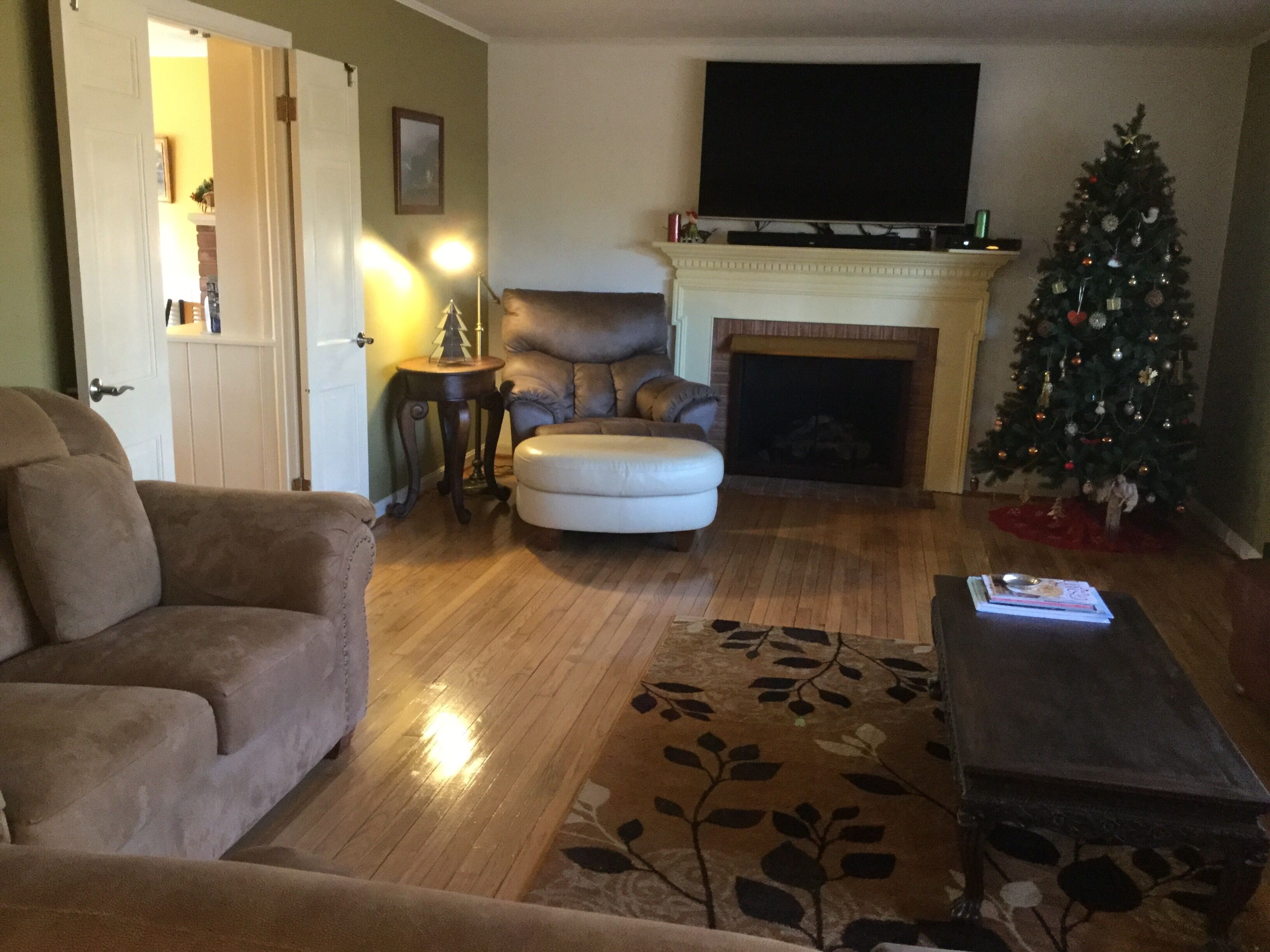 Een woonkamer met een open haard, een televisie erboven, een kerstboom en een bank.