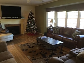A living room with a fireplace, a Christmas tree, a leather sofa, and a flat-screen TV.