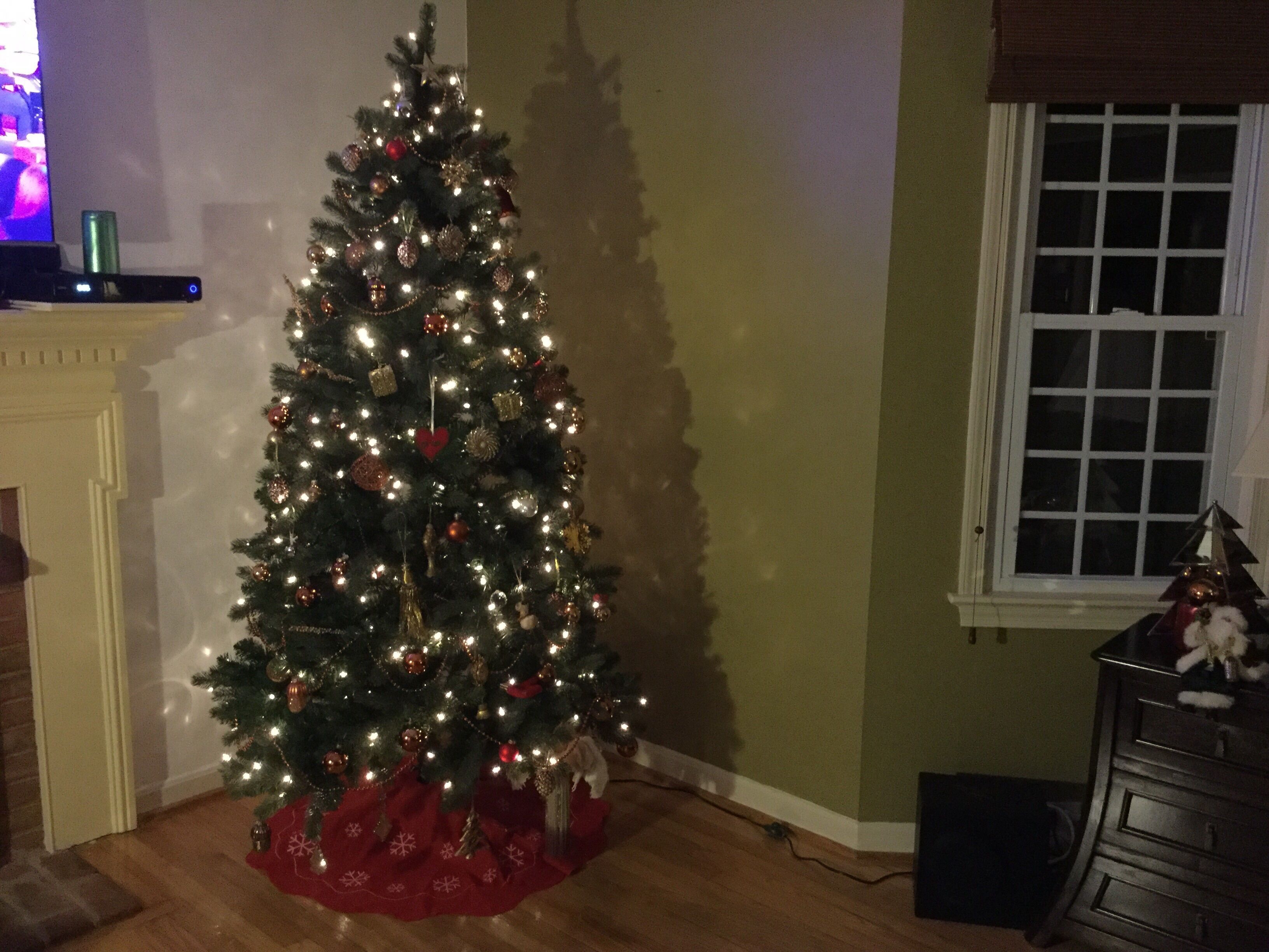 Un árbol de Navidad en un rincón de una habitación con una ventana y un aparador.