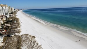A beach with white sand, clear blue water, and buildings along the shore.