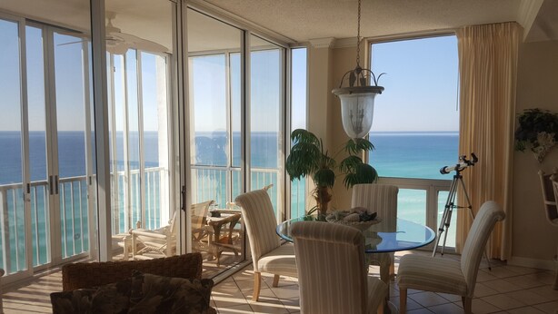 A balcony with a view of the ocean, furnished with chairs and a table, and a hanging light fixture.