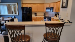 A kitchen with wooden cabinets, a black refrigerator, a stove, and two bar stools. - Tri-Cities Home Away From Home (Richland)