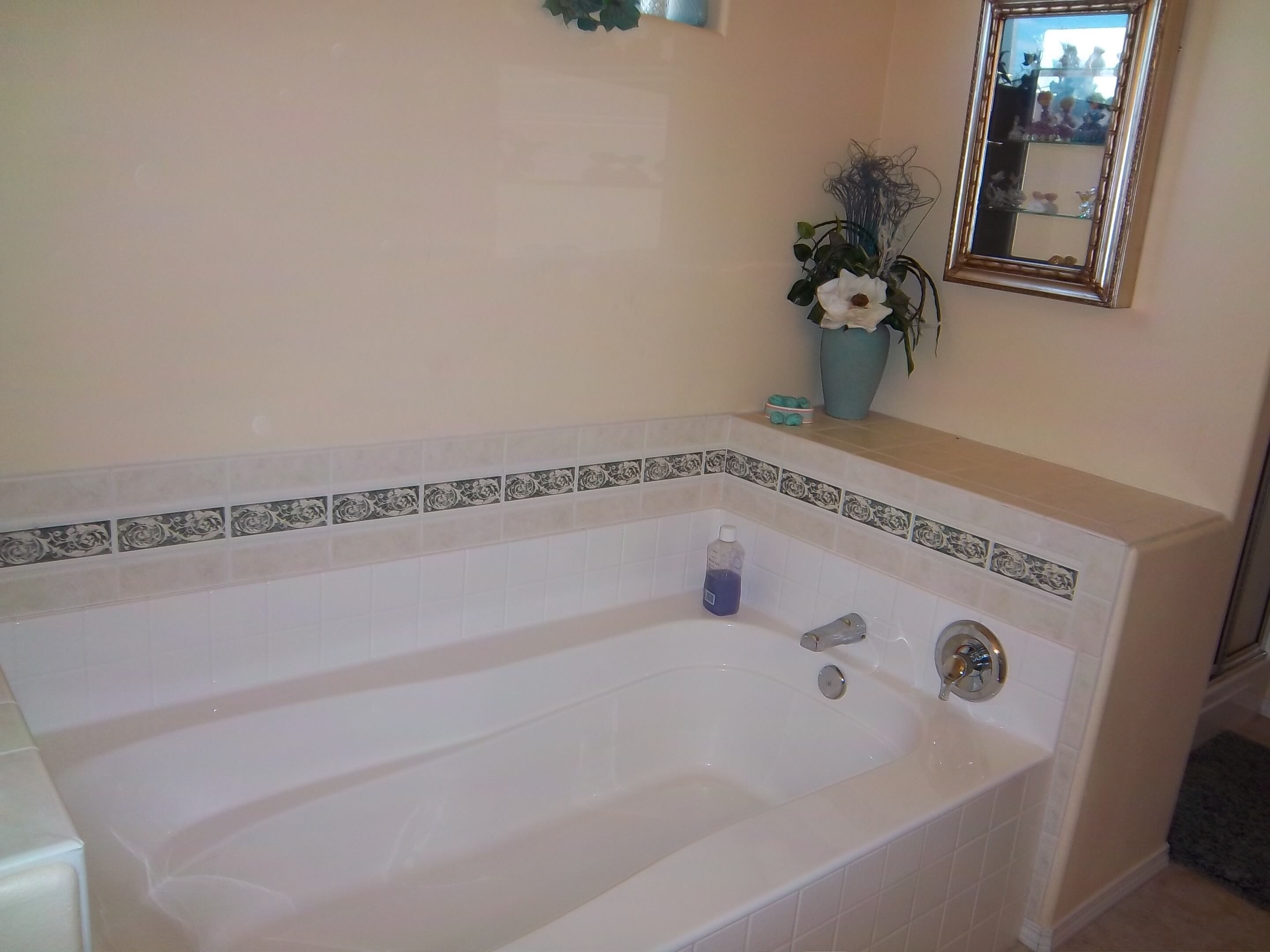 A bathroom with a white bathtub, a blue bottle, and a vase with flowers.